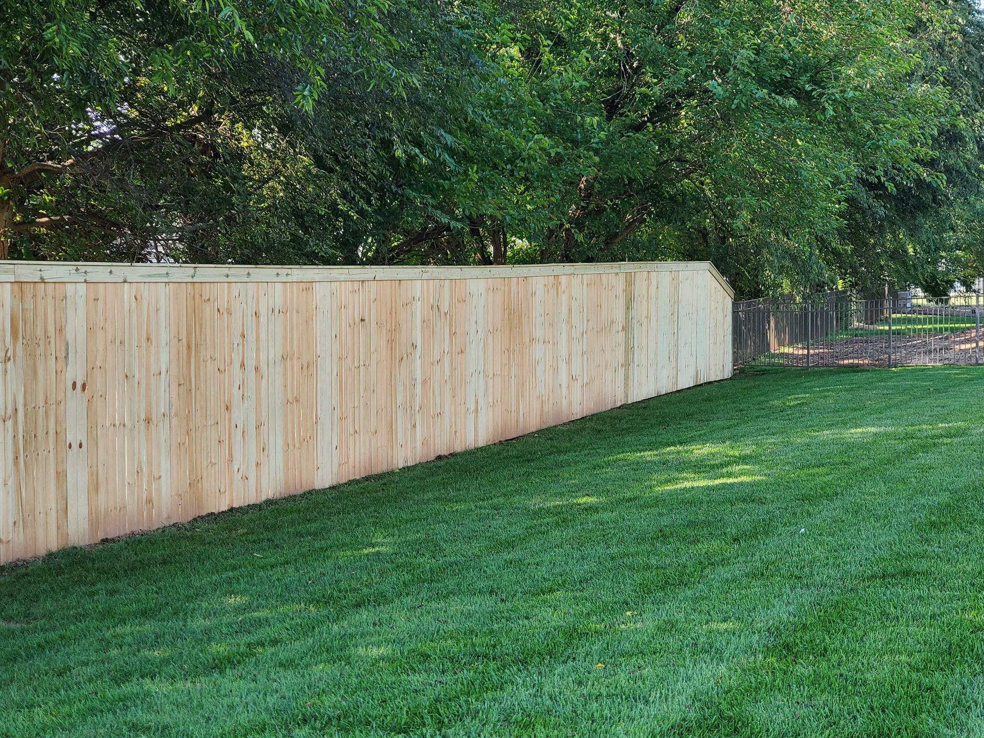 Wooden fence bordering a lush green lawn, trees in background.