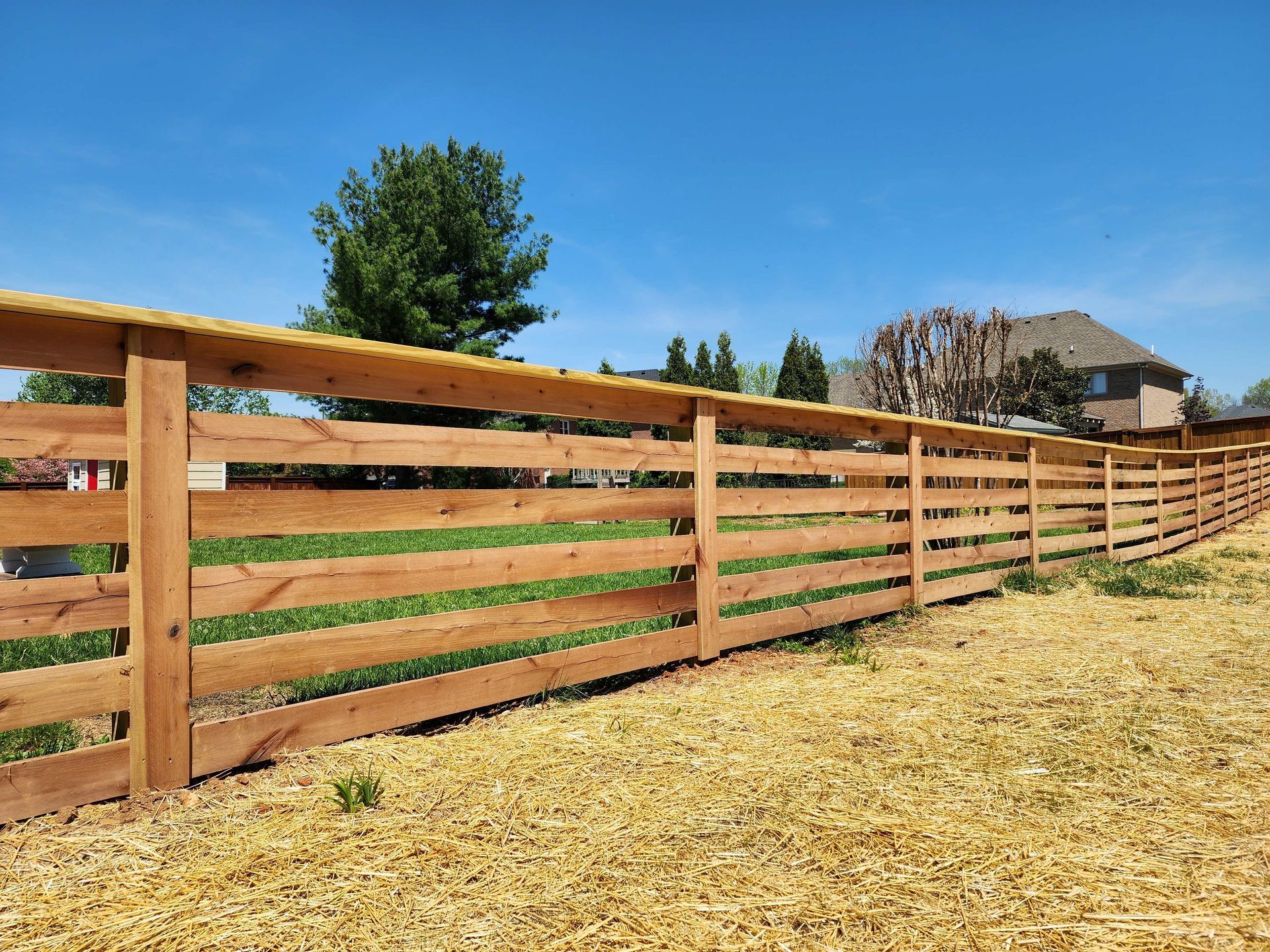 Wooden fence in a yard under a bright blue sky, with a house in the background.