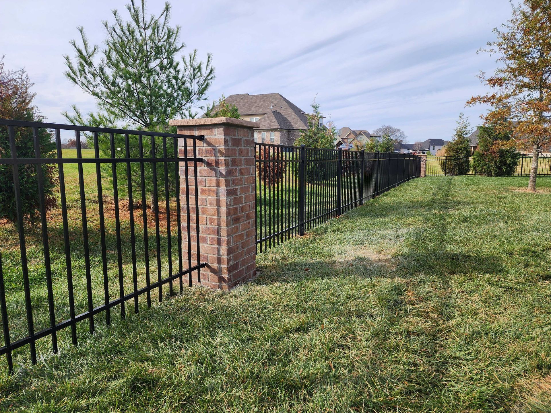 Black metal fence with brick pillar, enclosing a grassy backyard.
