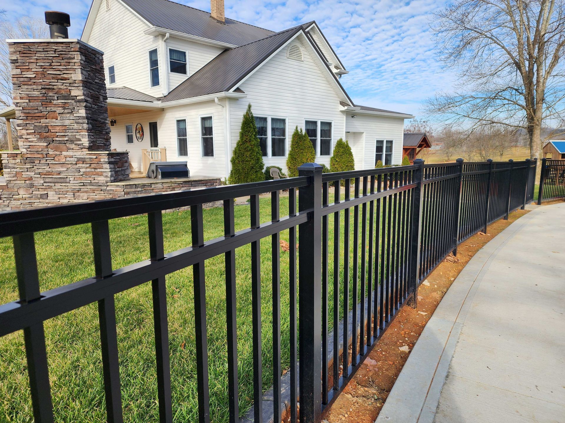 Black metal fence borders a grassy lawn, with a white house in the background.
