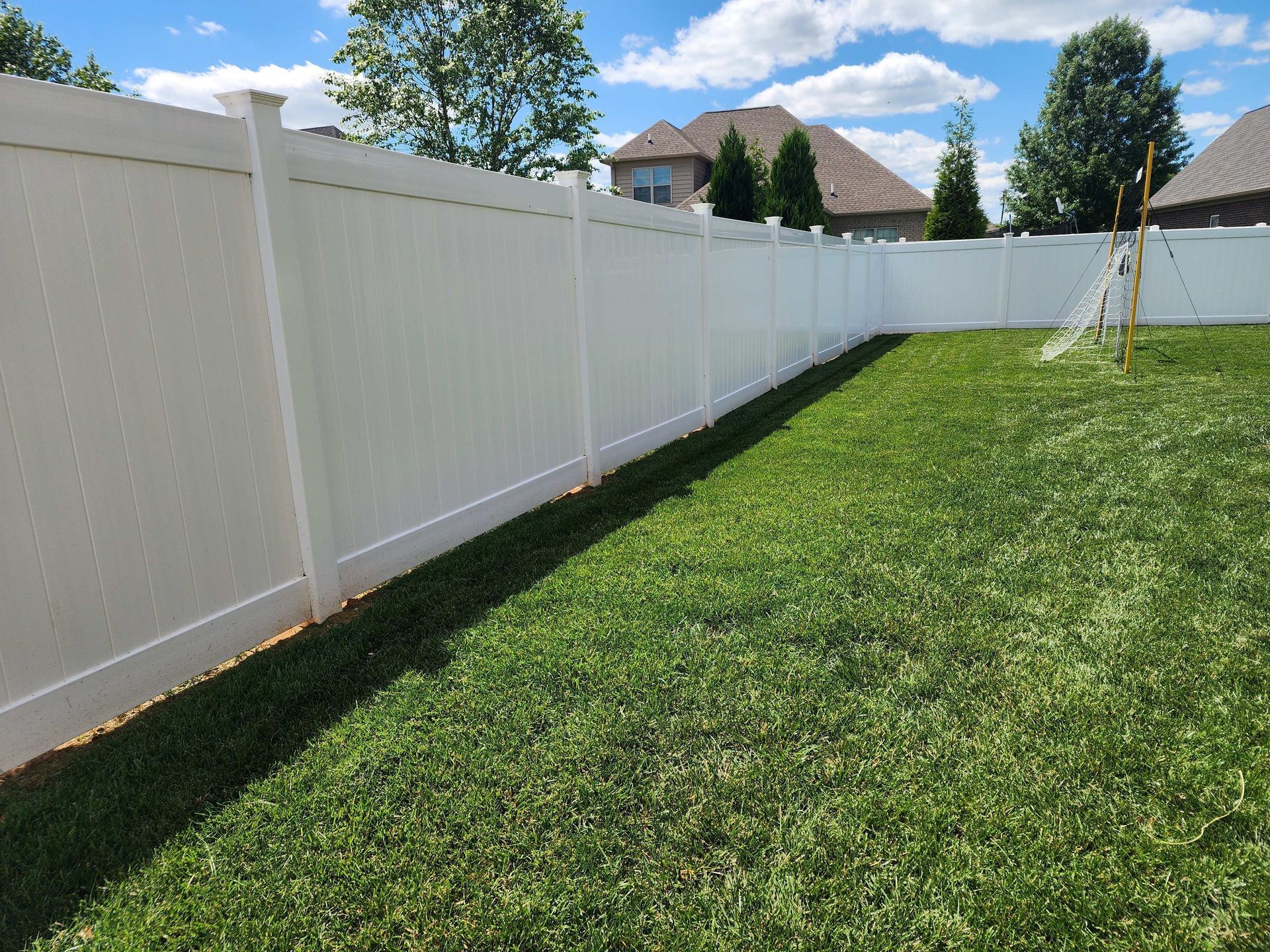 White vinyl fence enclosing a green lawn on a sunny day.