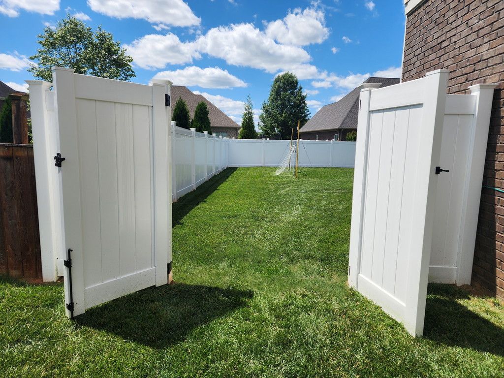 White gates open into a grassy backyard with a white fence and blue sky.