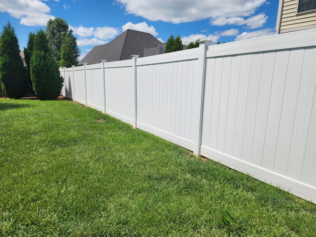 White vinyl fence in a green yard under a blue sky with some trees.