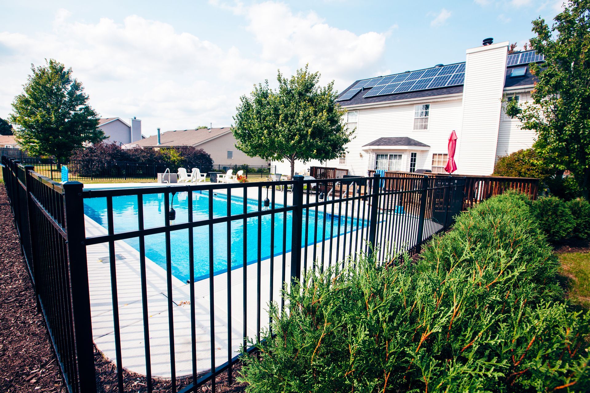 A fence surrounds a swimming pool with a house in the background