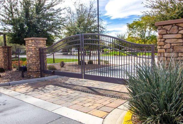A large wrought iron gate is surrounded by stone pillars and trees.