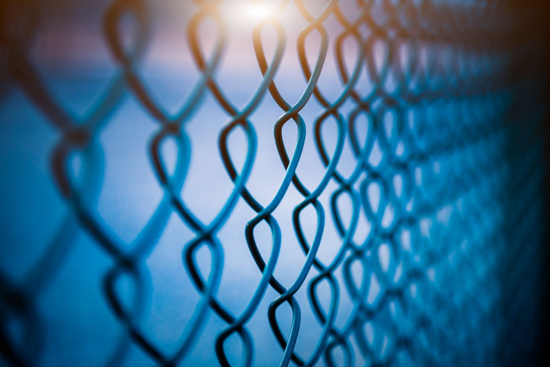 Blue chain-link fence, close-up with a soft, blurred background and a bright light source at the top.