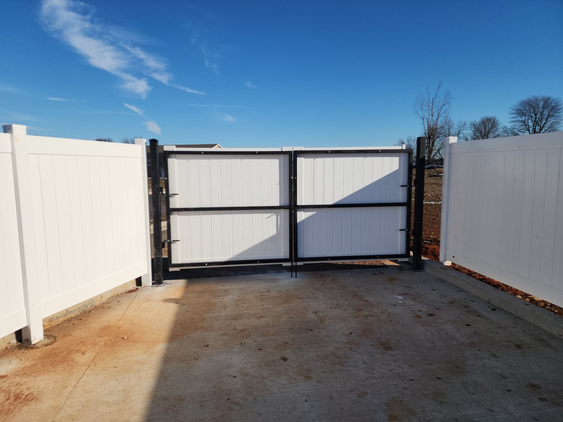 White vinyl fence with a black metal gate against a blue sky.