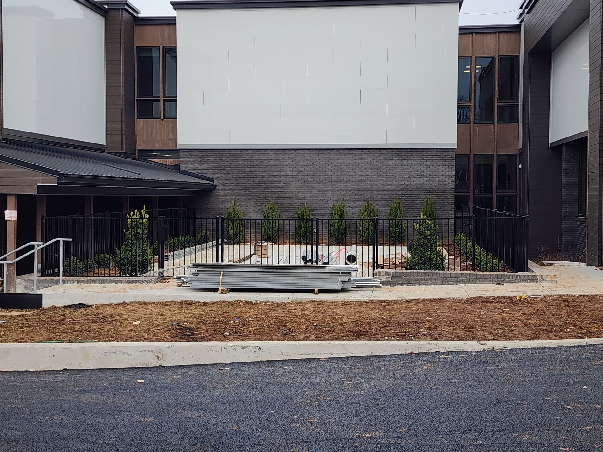 Exterior of a building with a black fence, small trees, and a ramp. Brown and white walls.