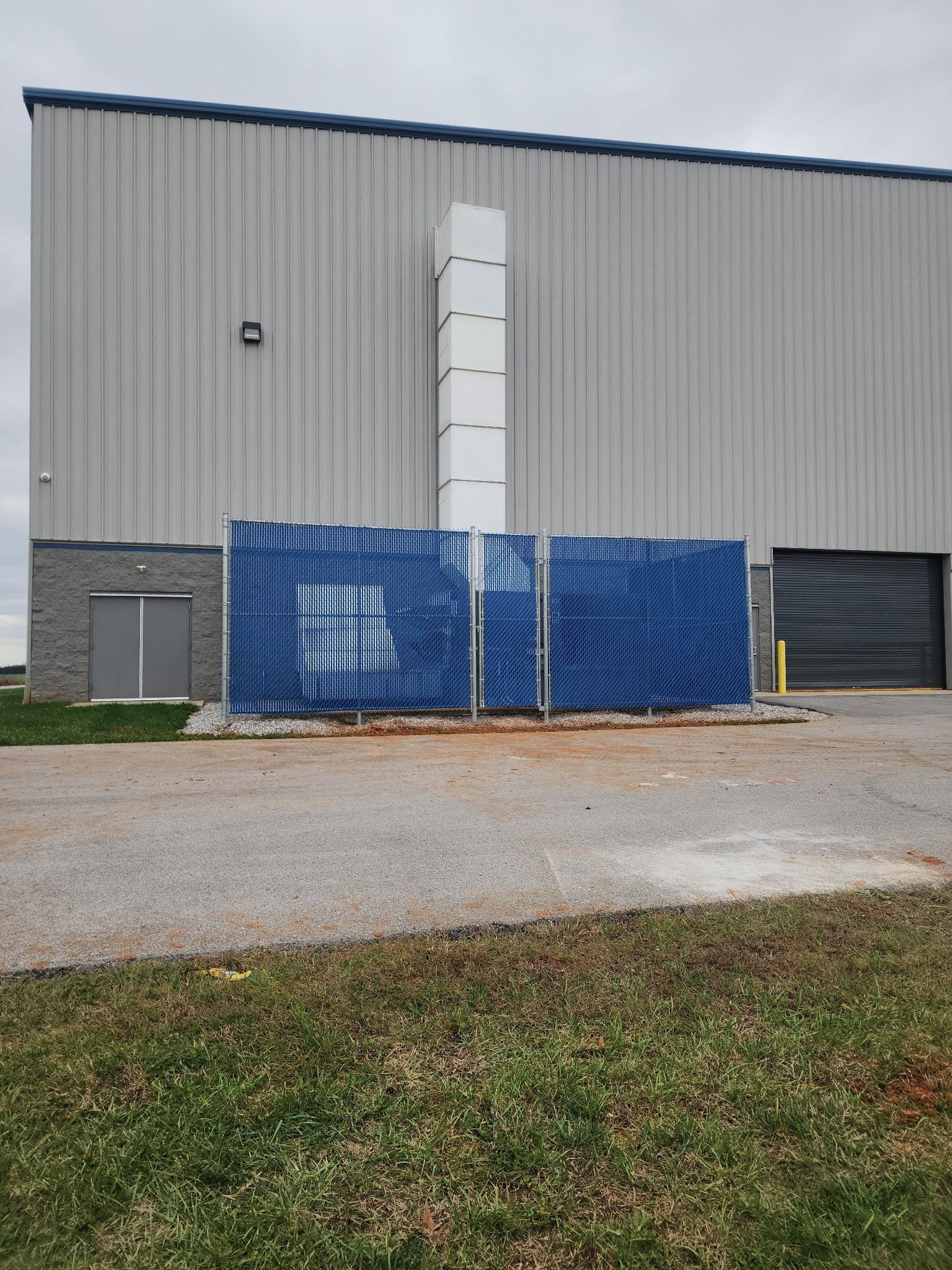 A blue fenced area in front of a tall, metal industrial building with a white chimney.