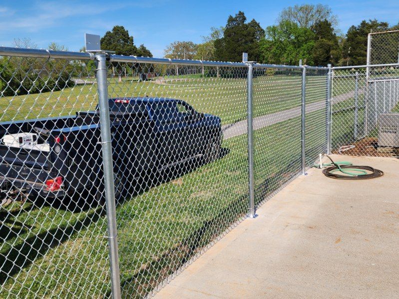 Chain link fence surrounding a concrete area with a black pickup truck in the background on a grassy area.