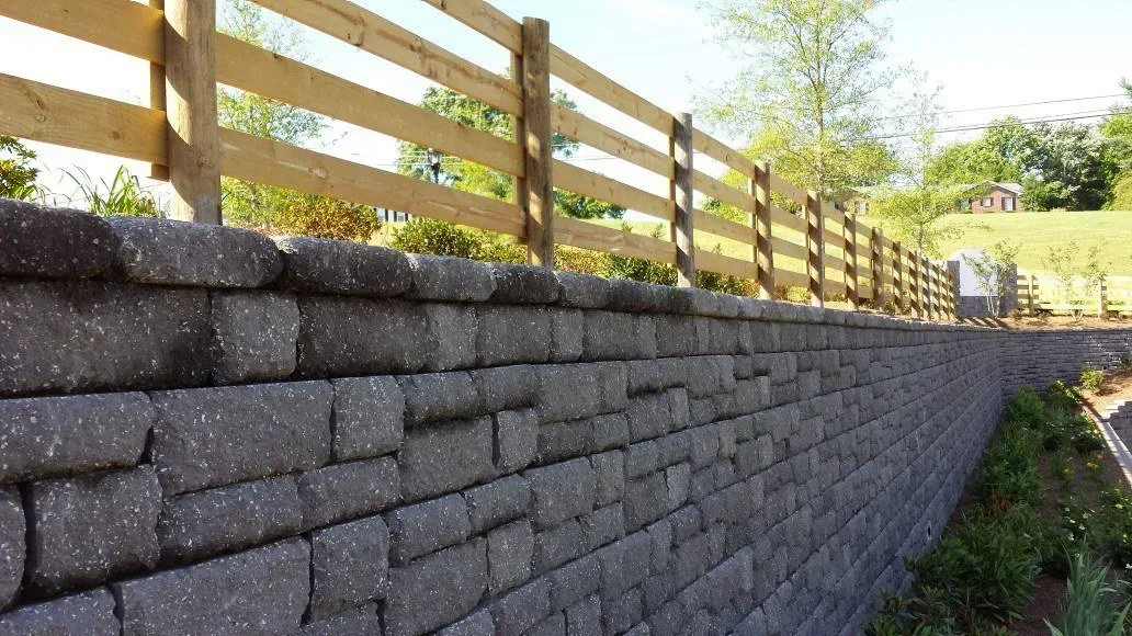 A brick wall with a wooden fence behind it.