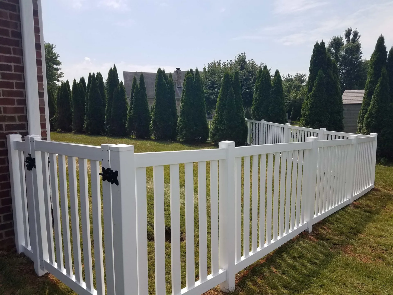 White picket fence surrounding a grassy yard with evergreen trees in the background. White picket fence surrounding a grassy yard with evergreen trees in the background.