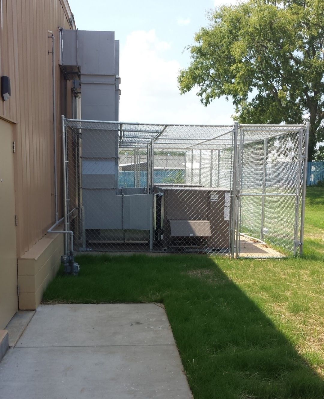 Metal HVAC equipment enclosed in a chain link fence outside a building.