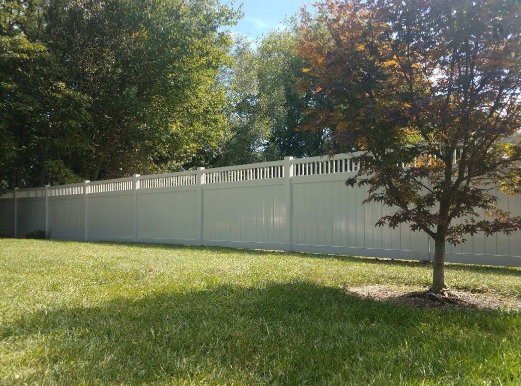 White vinyl fence in a grassy yard with trees under a blue sky.