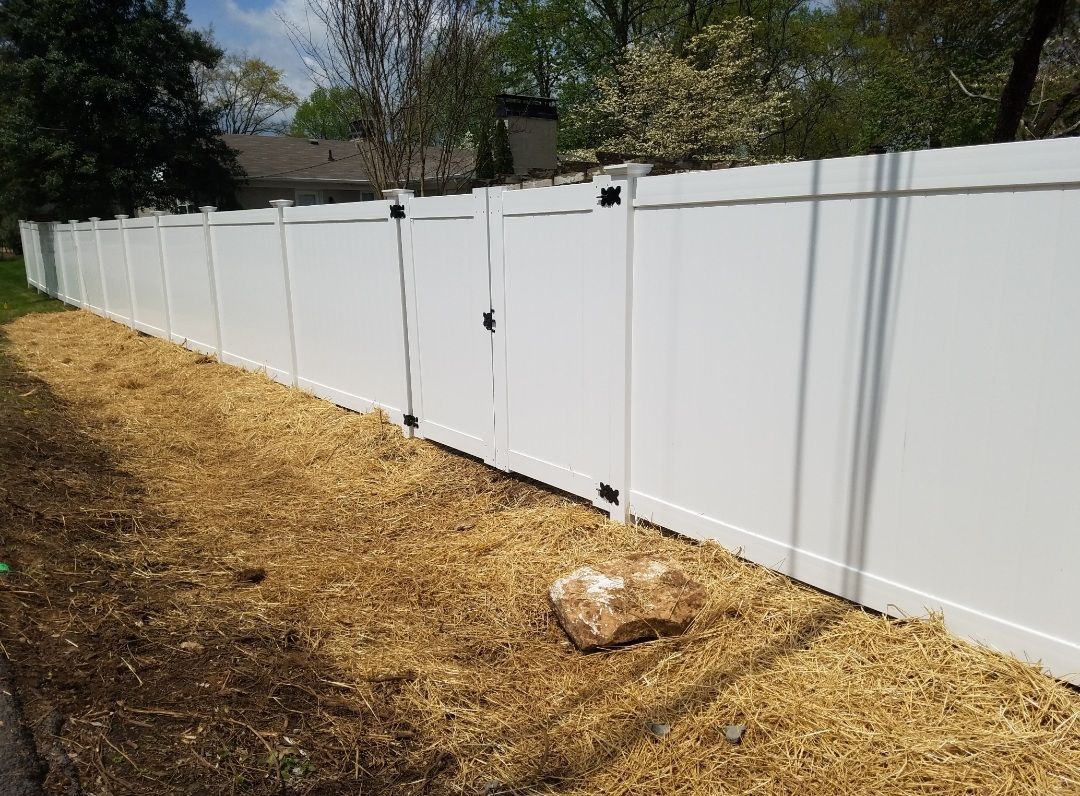 White vinyl fence along a lawn covered in mulch and a large rock.