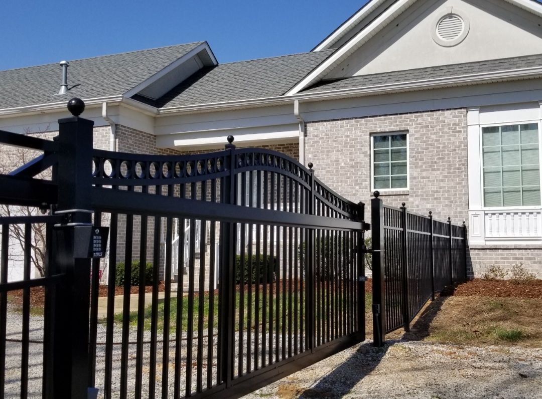 Black metal gate in front of a light brick house with a gray roof and white trim.
