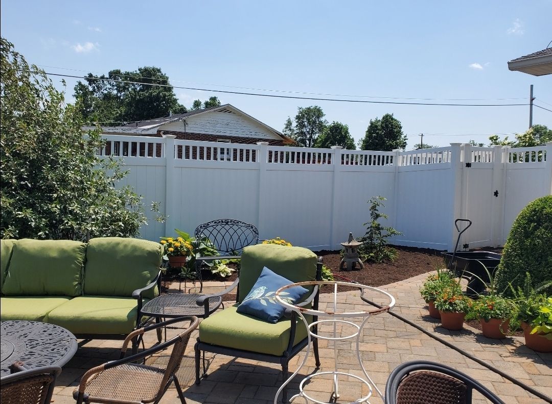 Backyard patio with green seating, brick pavers, white fence, and potted plants.