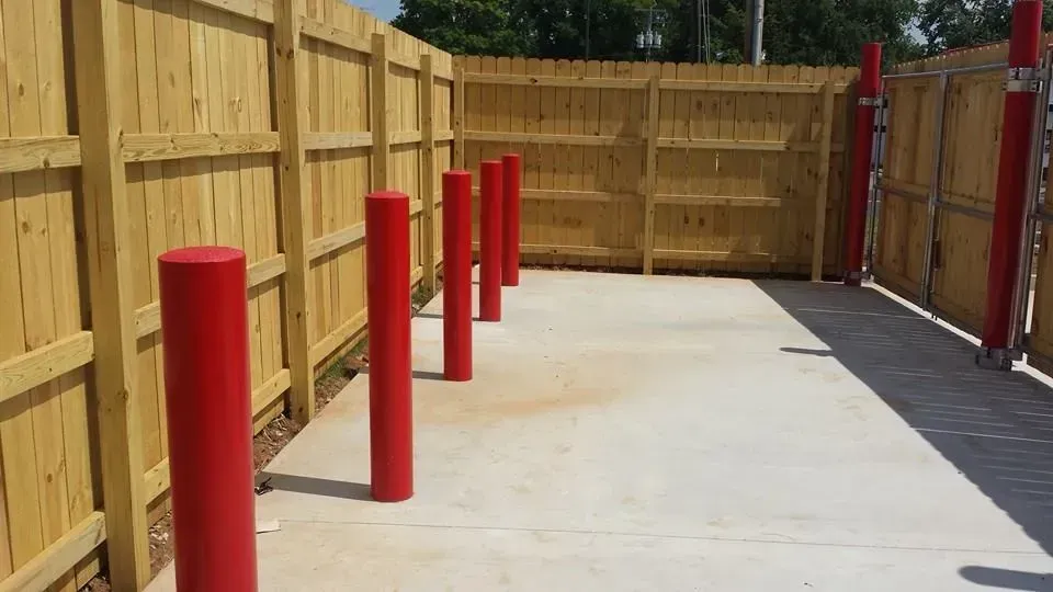 Red bollards line a concrete area bordered by a wooden fence.