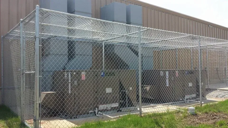 Chain-link fence encloses industrial HVAC equipment; exterior of a building.