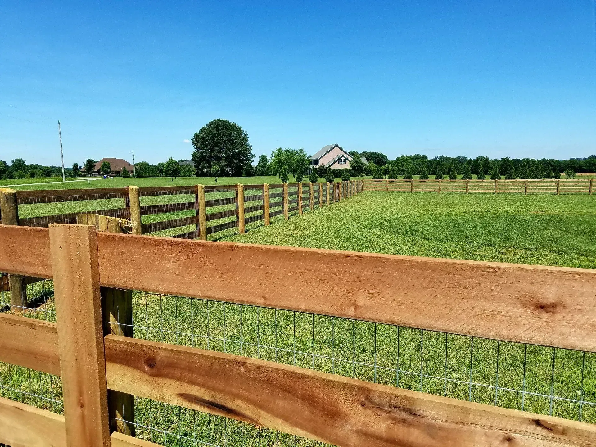 A wooden fence surrounds a grassy field with a house