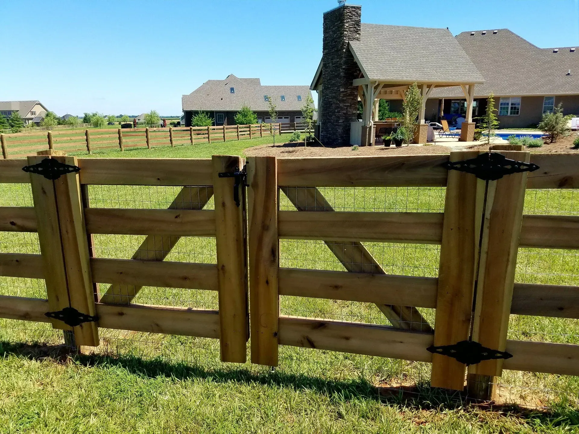 Wooden gate in a grassy field, leading to a house with a stone chimney.