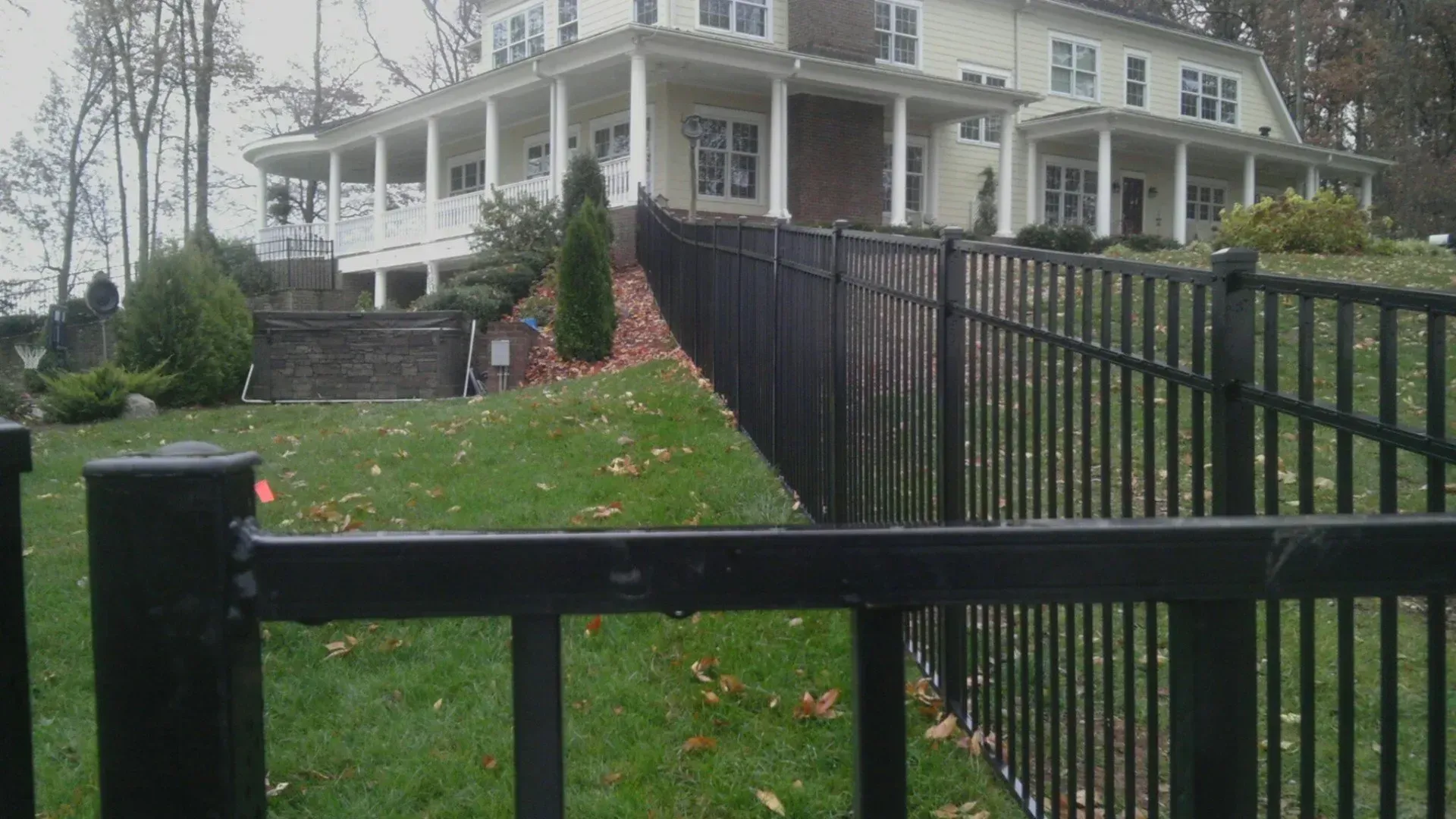 Black metal fence in front of a large beige house on a grassy hill.
