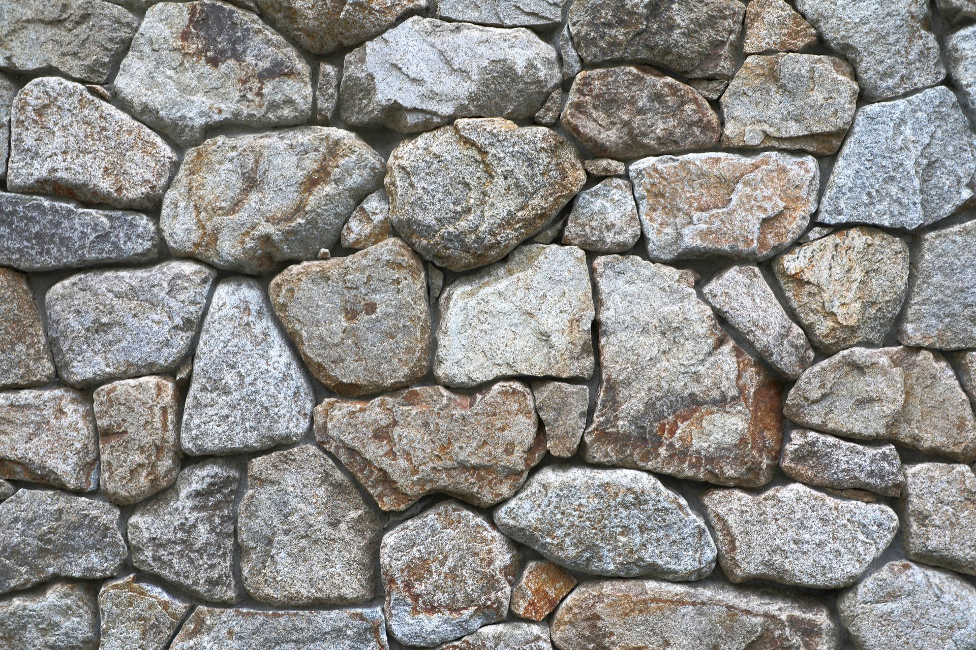 Rustic stone wall close-up with tightly fitted rocks of varied shapes and sizes, natural texture.
