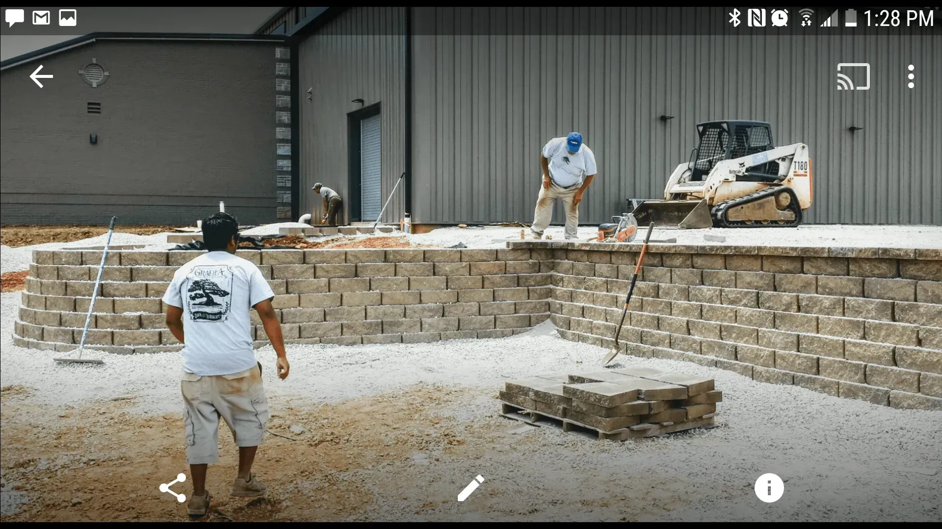 A man is standing in front of a brick wall with a bulldozer in the background.