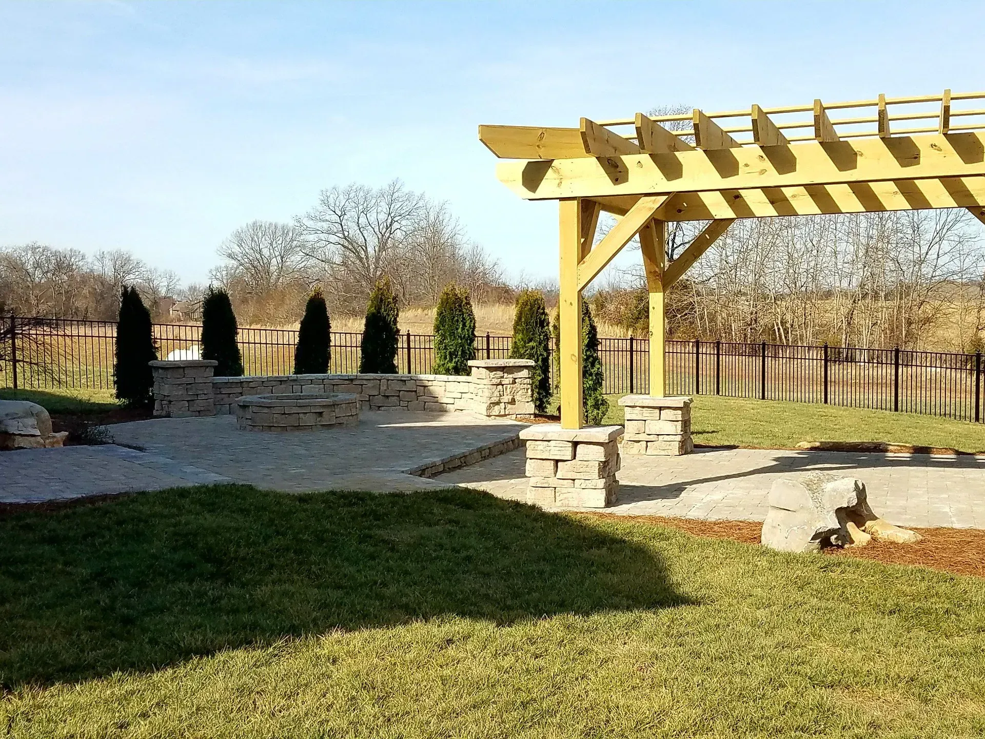 A wooden pergola is sitting in the middle of a lush green yard.
