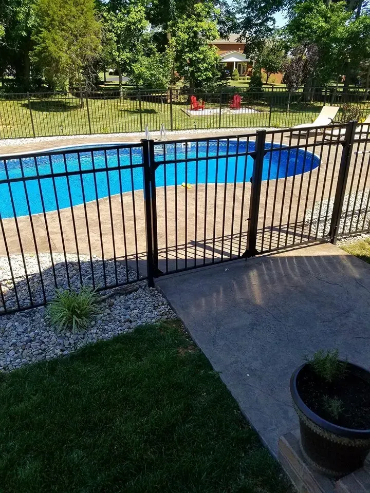 Black fenced-in blue pool, patio, and grass in a backyard setting.