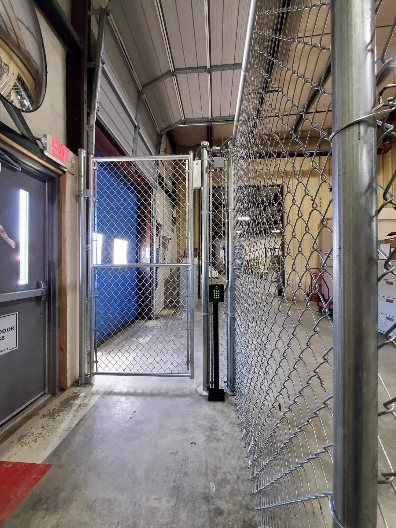 A chain-link fence and gate in a building's interior hallway, alongside a blue door, and an exit door.