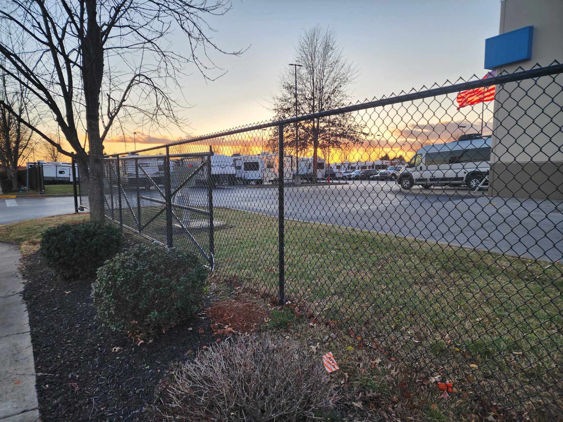 Black chain-link fence with a park in the background. Sunset in the sky.