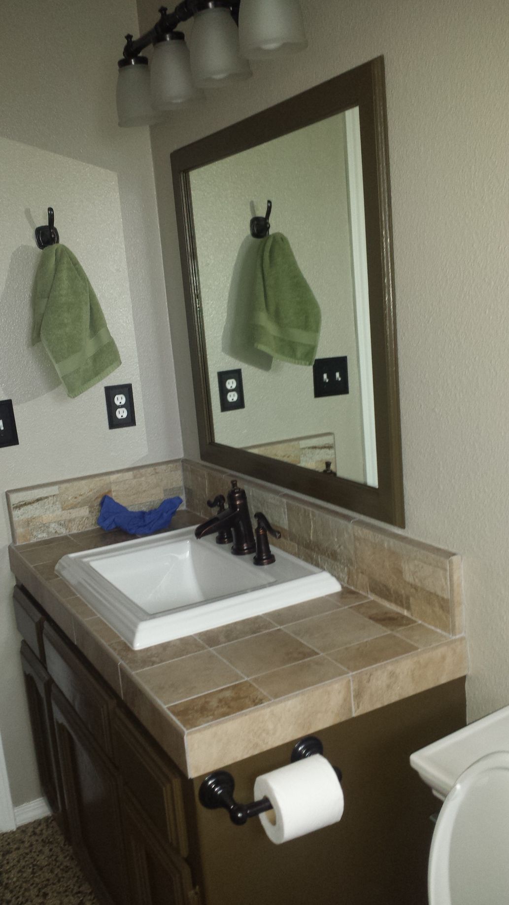 A bathroom with a sink , toilet , mirror and towels hanging on the wall.
