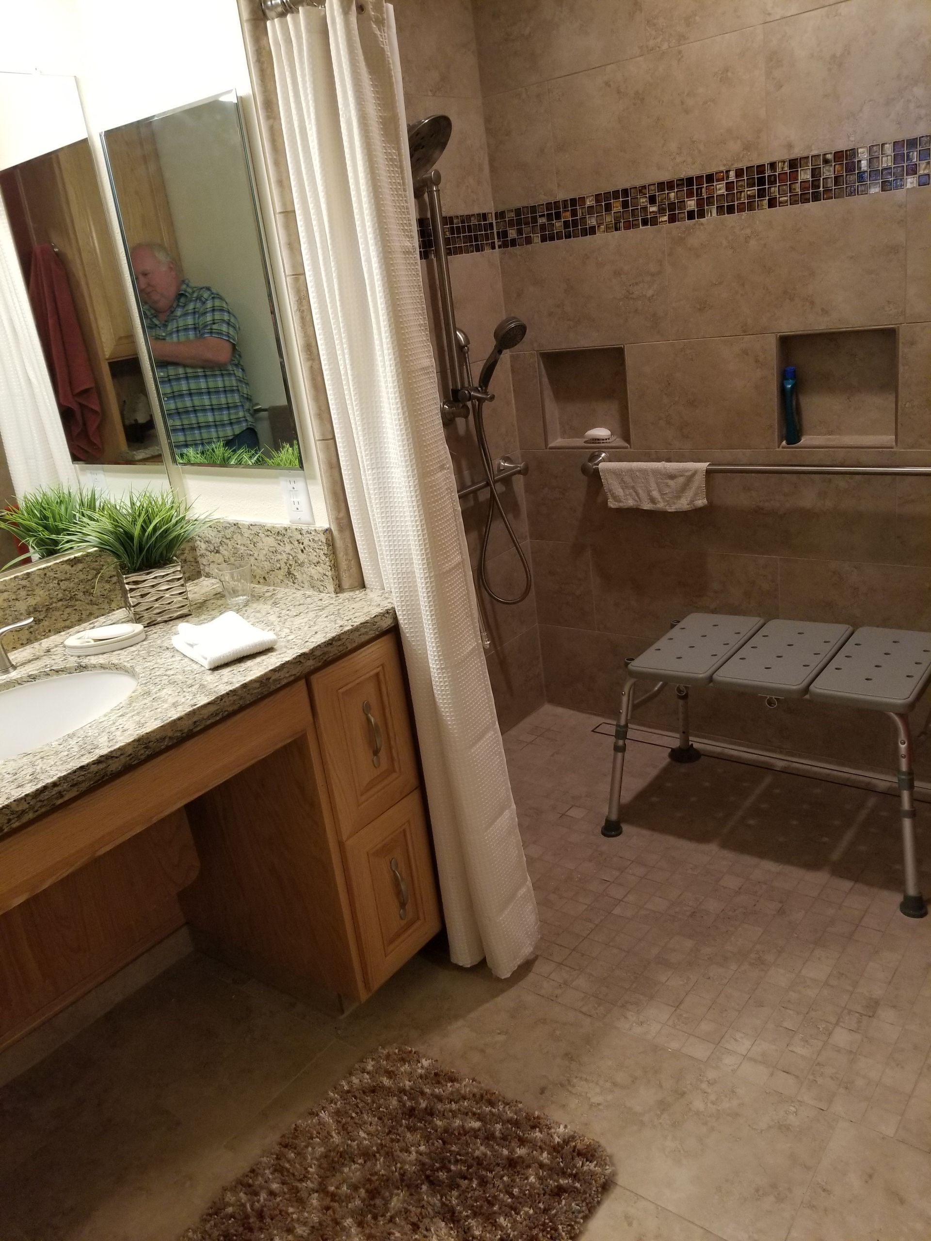 A bathroom with a sink , shower , bench and mirror.