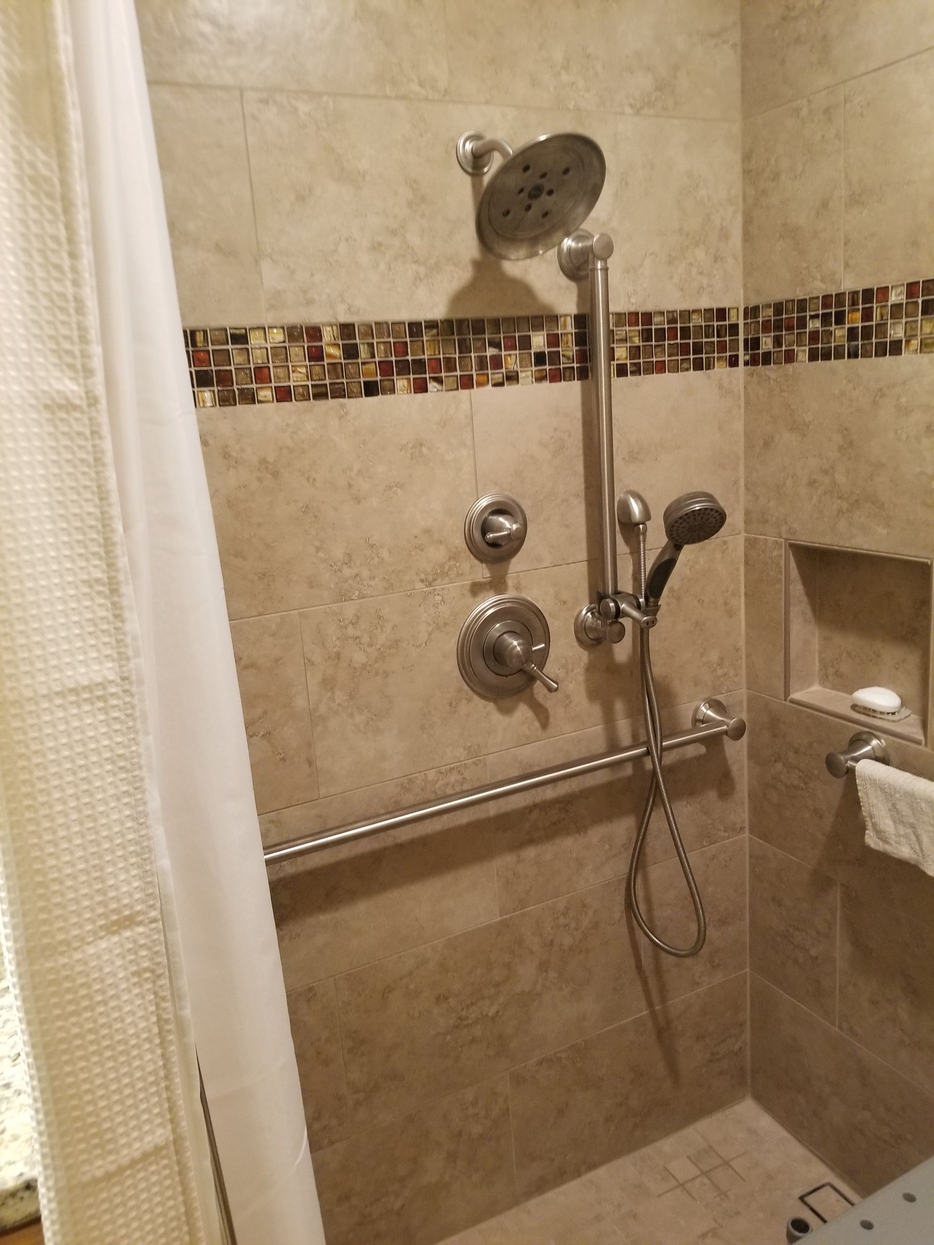 A bathroom with a walk in shower with a hand rail and a shower head.