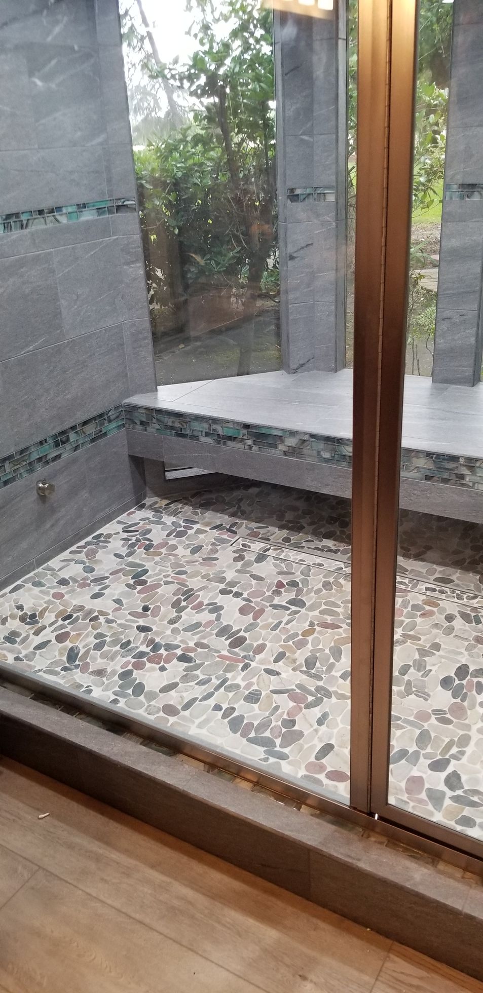 A walk in shower with a tiled floor and a large window.