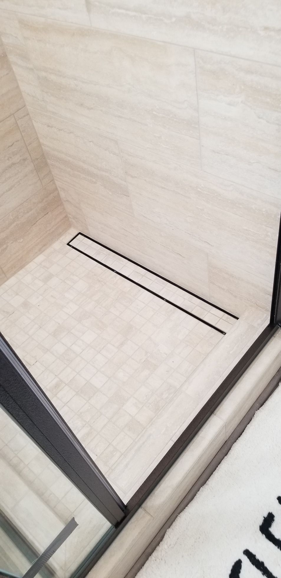 A bathroom with a walk in shower with a drain on the floor.