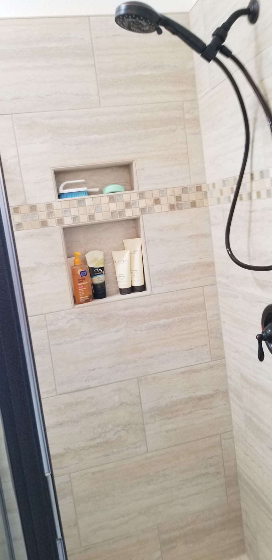 A shower with a built in shelf and a shower head.