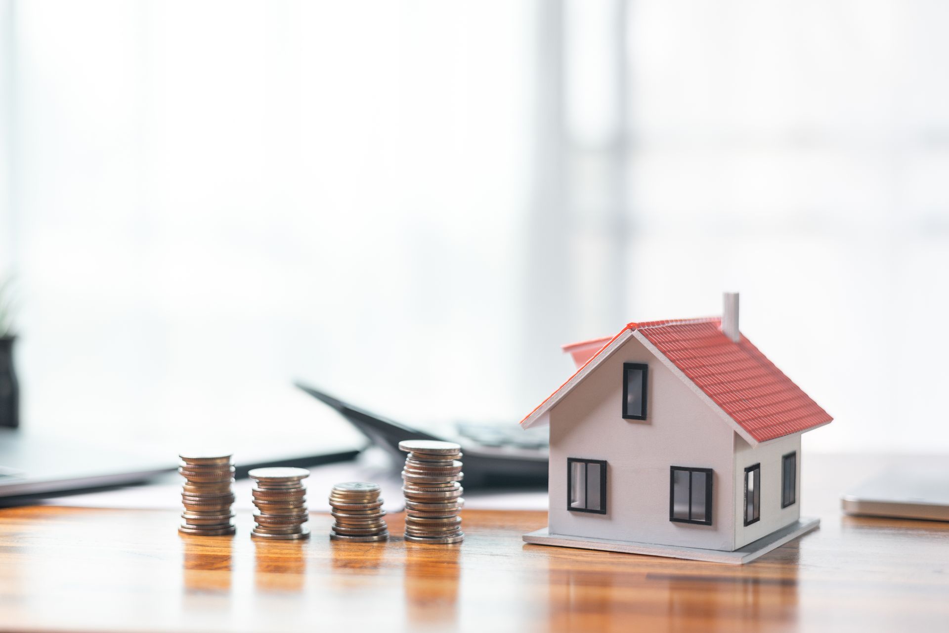 A model house is sitting on a wooden table next to stacks of coins.