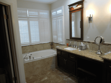 A bathroom with a jacuzzi tub , sink , mirror and shutters.