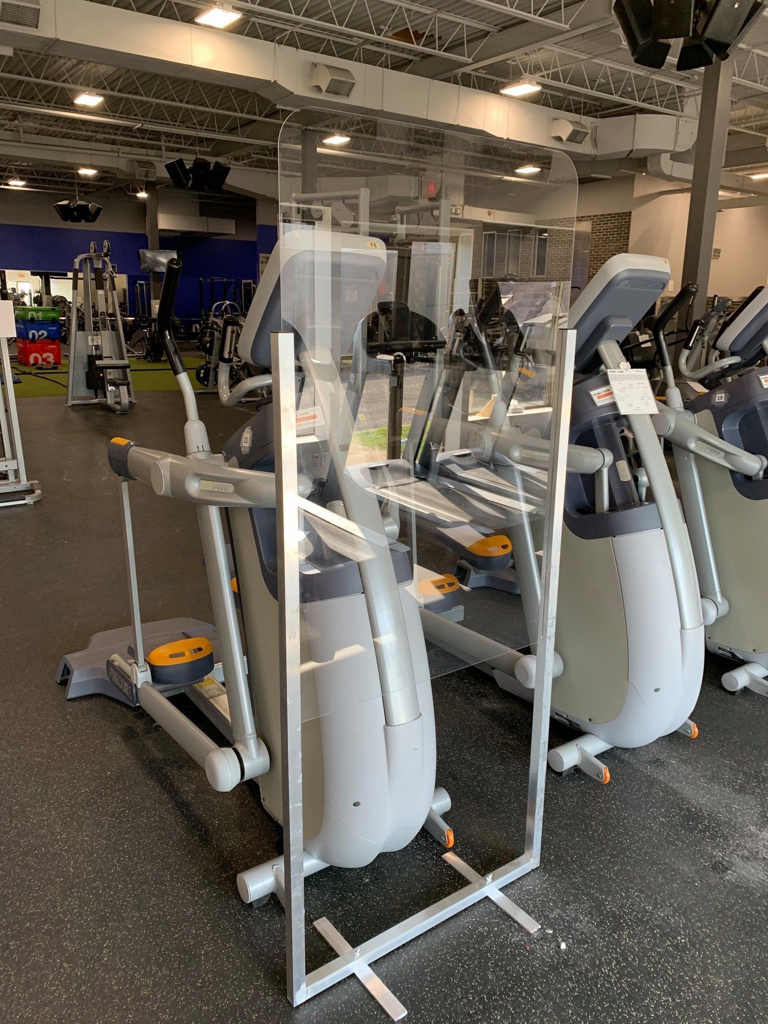 A gym with a lot of exercise equipment and a clear barrier.
