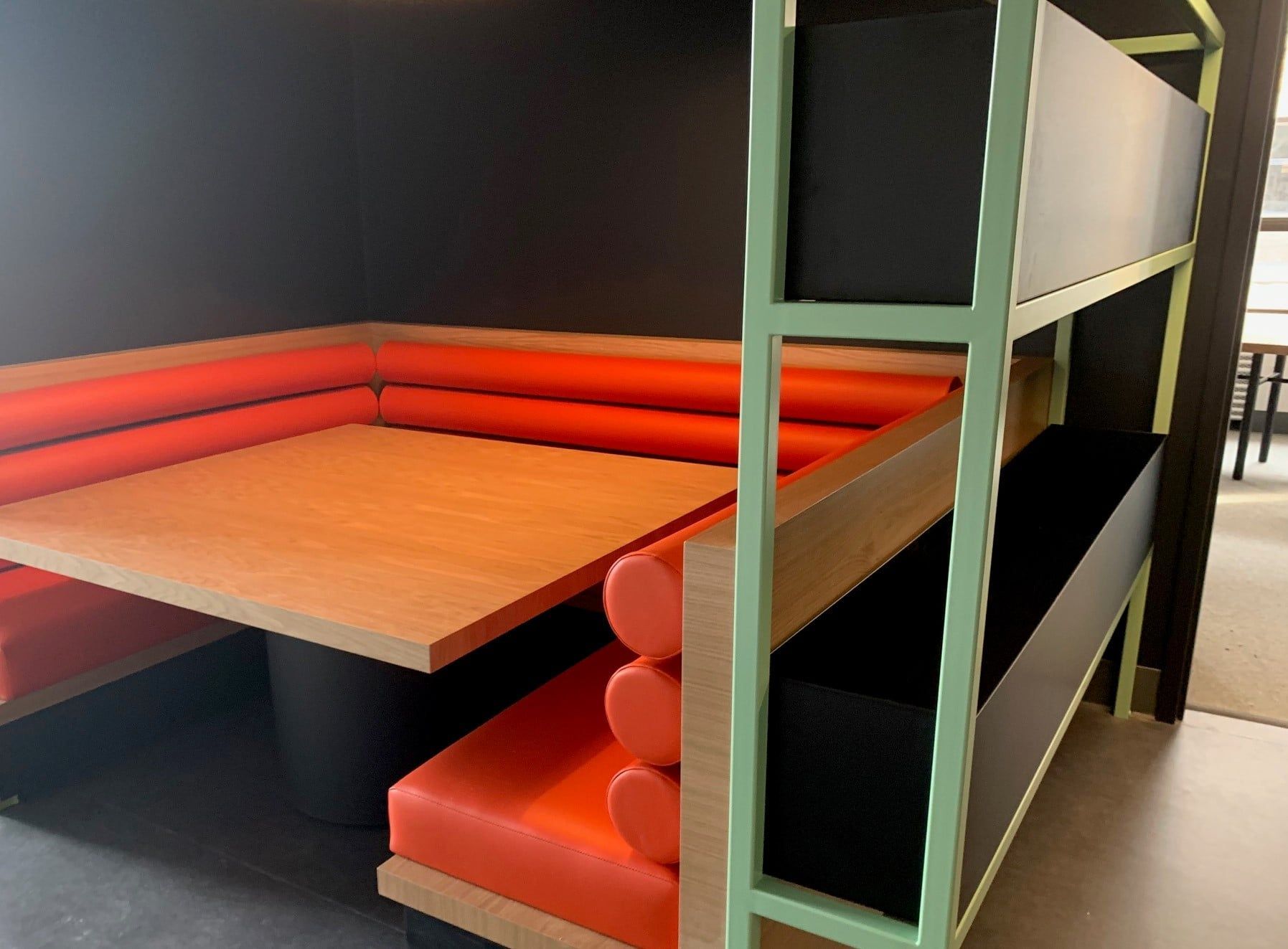 A restaurant booth with orange cushions and a wooden table