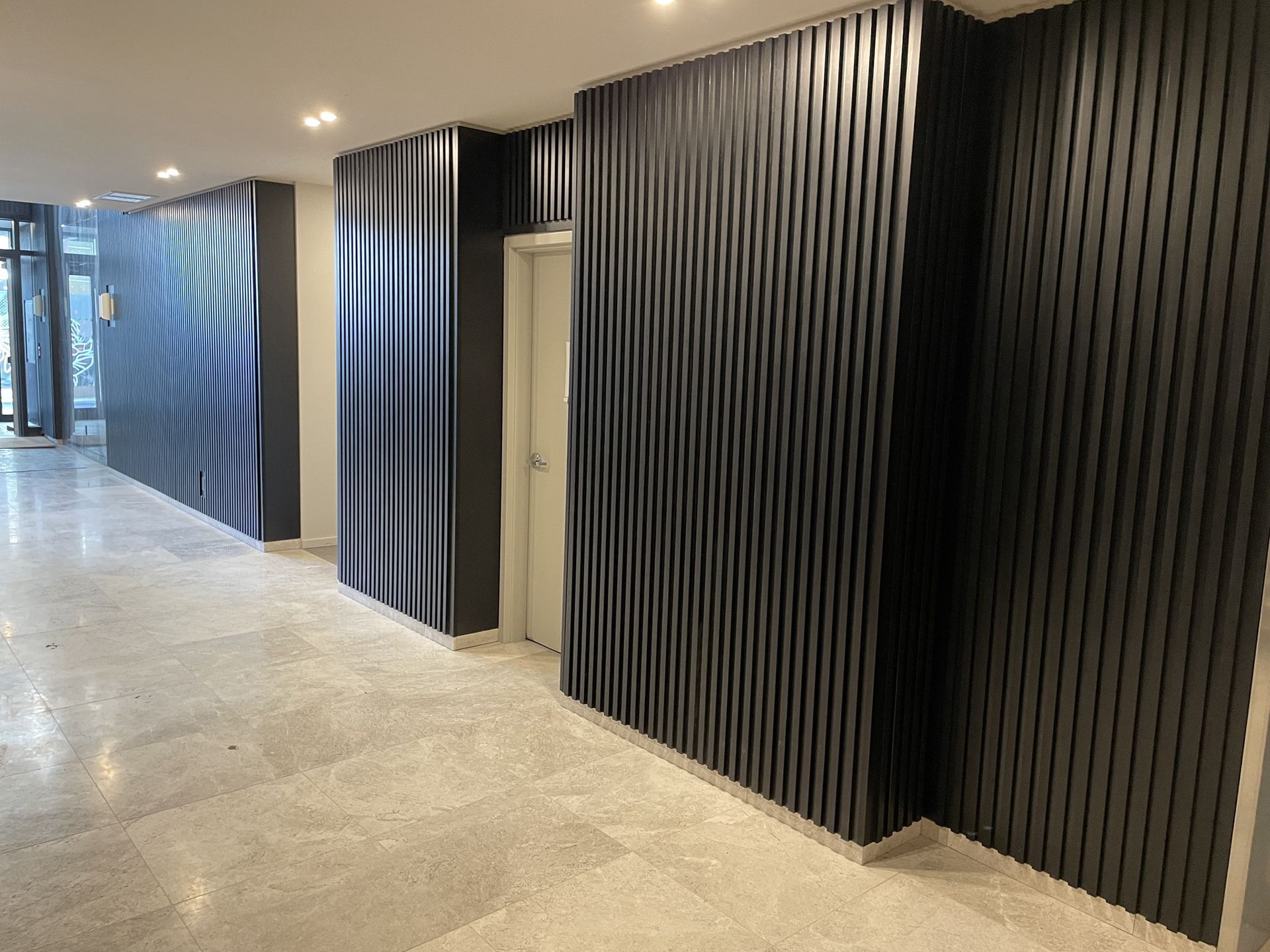 A long hallway with black walls and a white door.