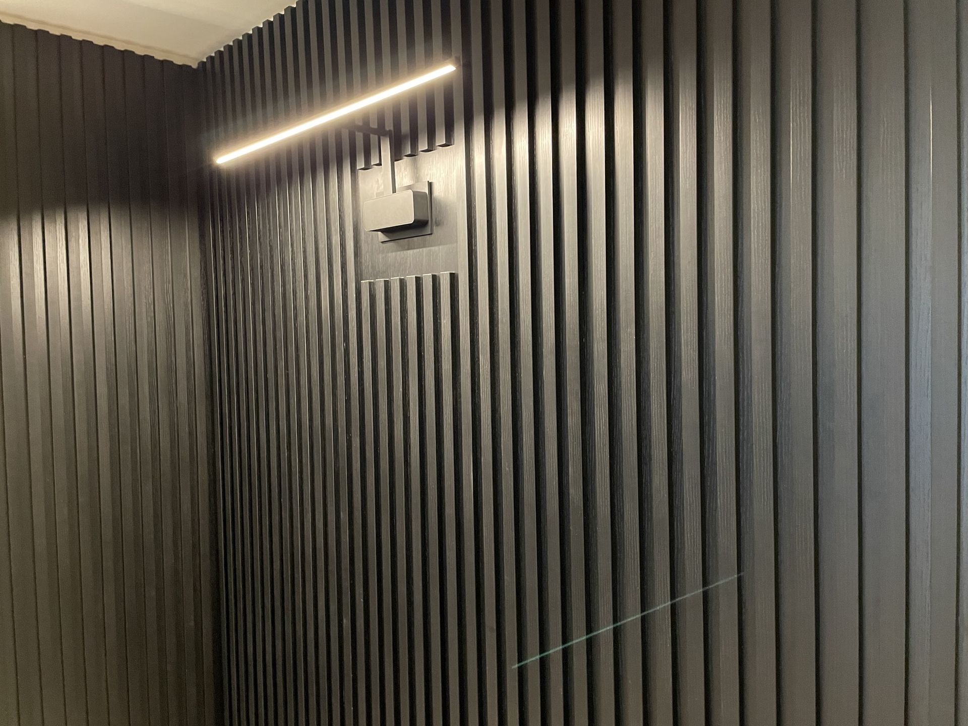 A black wall with a light on it and a clock on it.