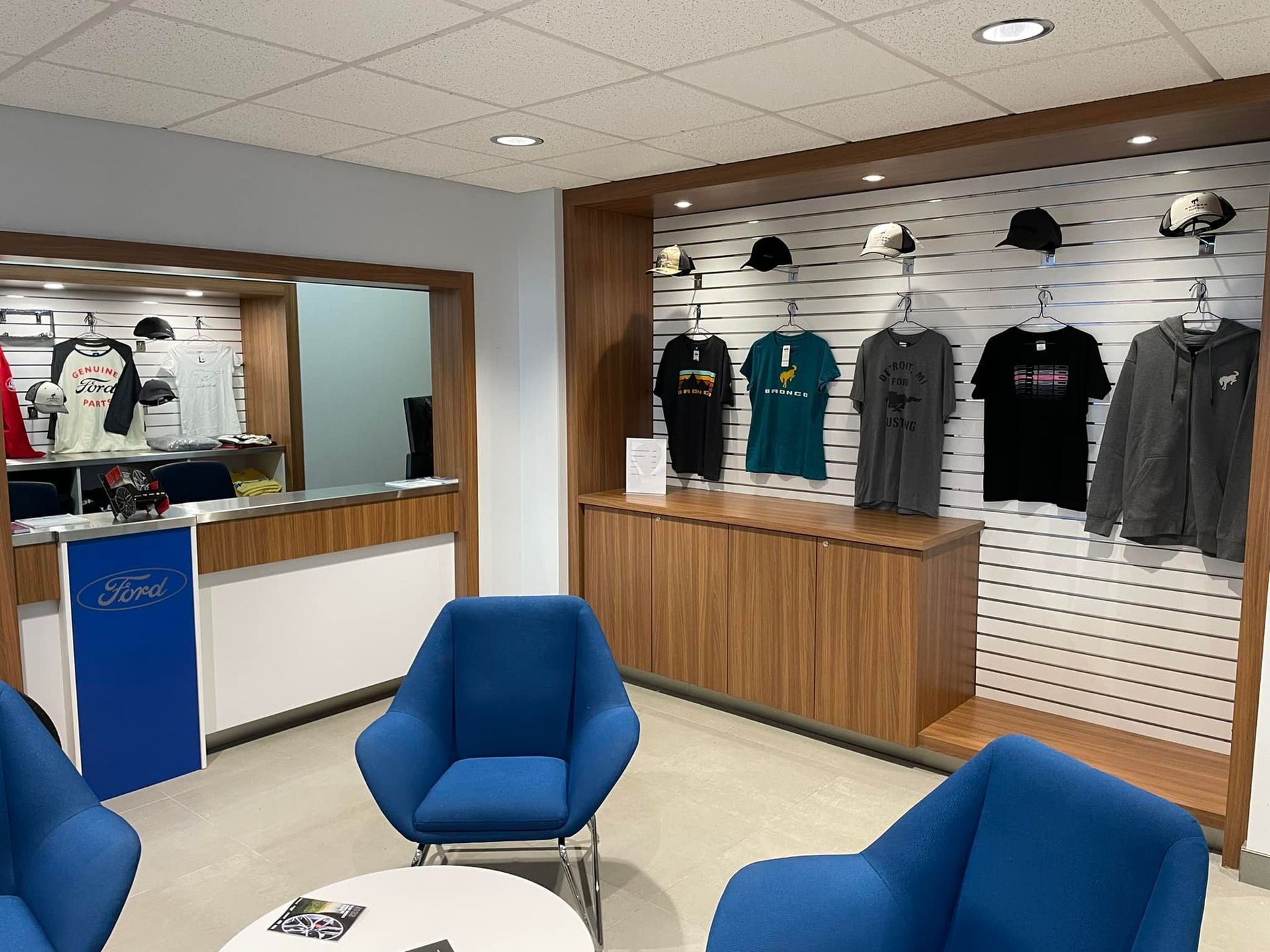 A room with blue chairs , a table , and a wall of t-shirts.