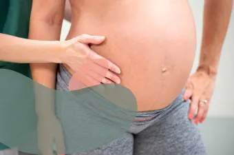 En persons hånd palperer magen til en gravid person for å vurdere fosterets stilling.