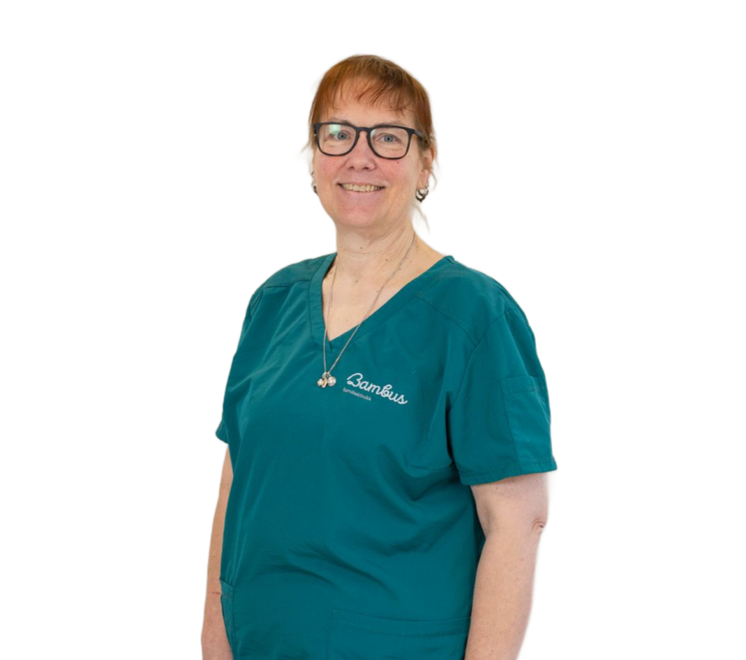 En person i en blågrønn skrubbtopp med logo, med briller og et enkelt halskjede, smiler mot en hvit bakgrunn.