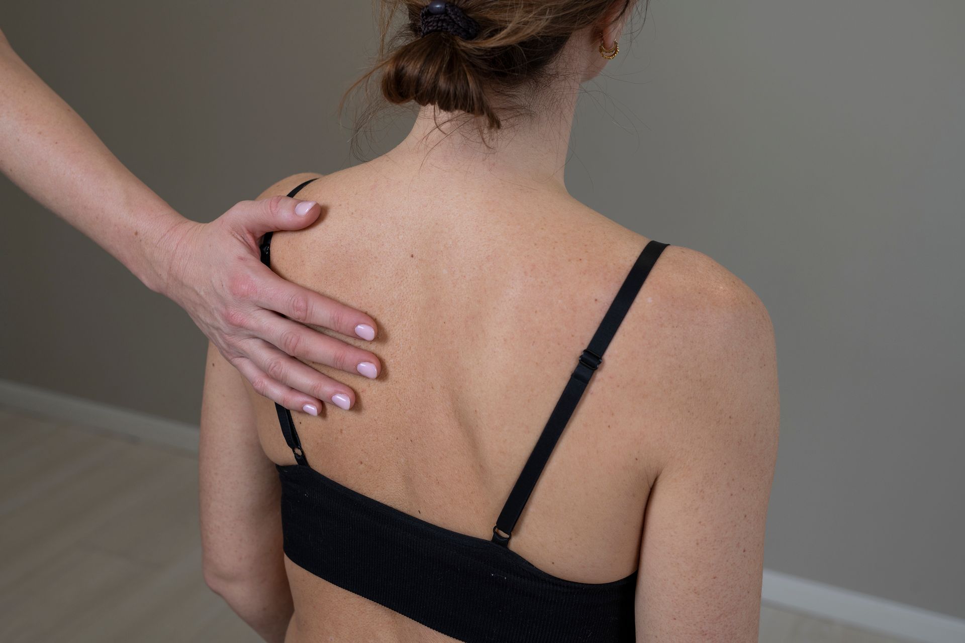 En hånd hviler på en persons øvre del av ryggen, sannsynligvis som et eksempel på en setting for fysioterapi eller medisinsk undersøkelse.