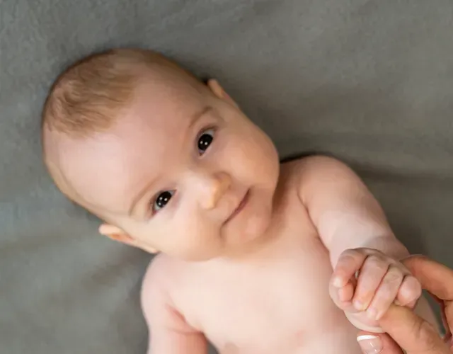 En baby som ser oppover mot kameraet mens den holder en voksens finger.