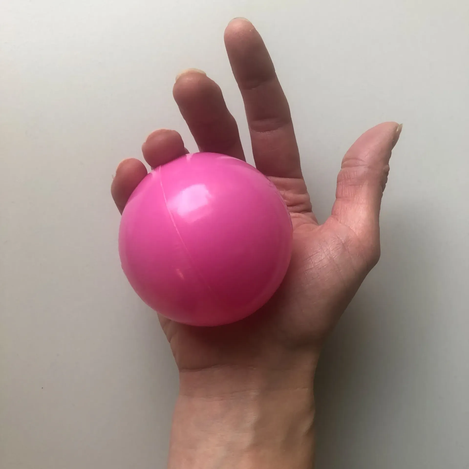 En hånd holder en glatt, knallrosa ball mot en vanlig, lys bakgrunn.